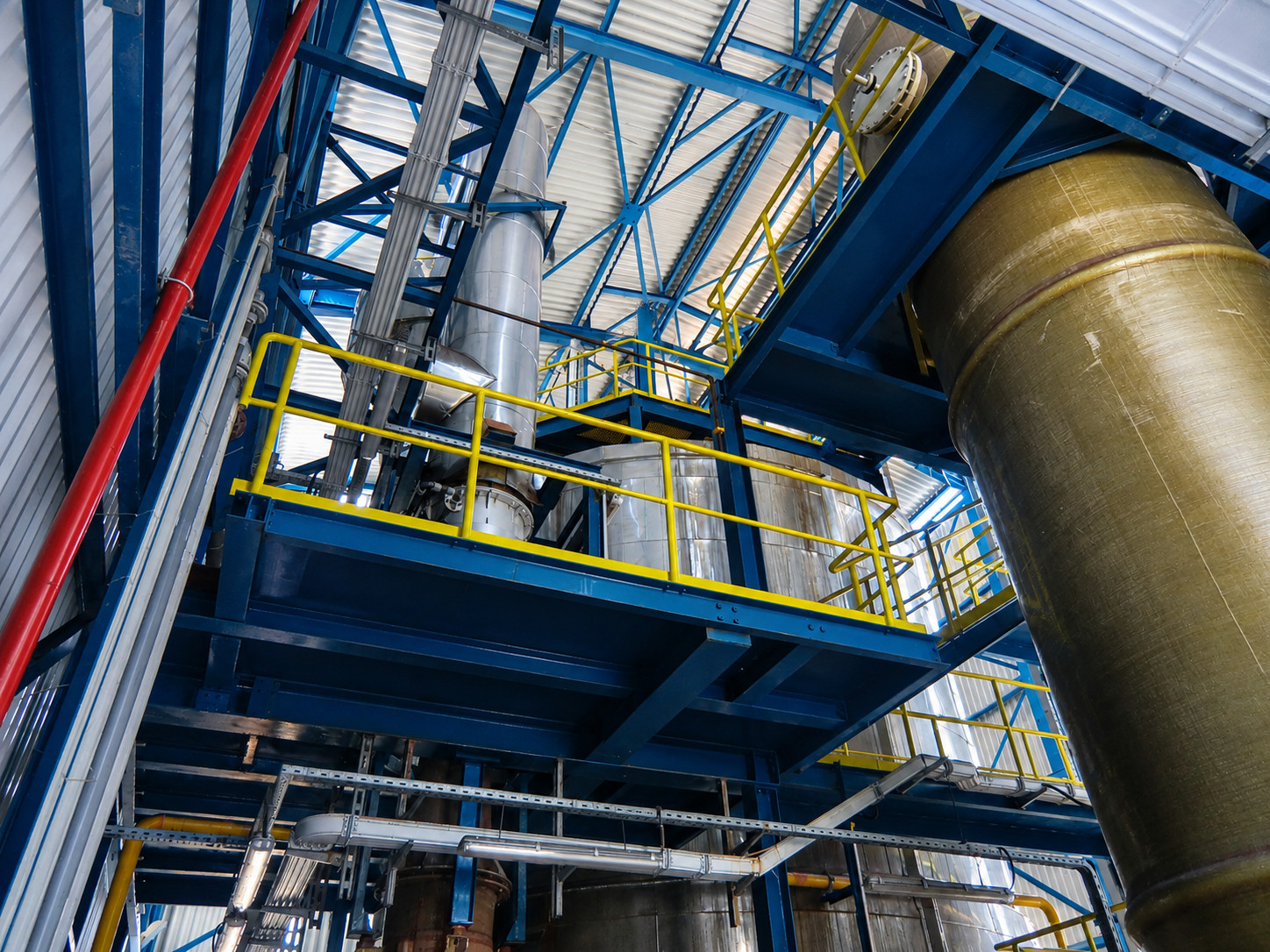Industrial spray roster manufacturing facility with steel structures, pipes, and yellow safety railings